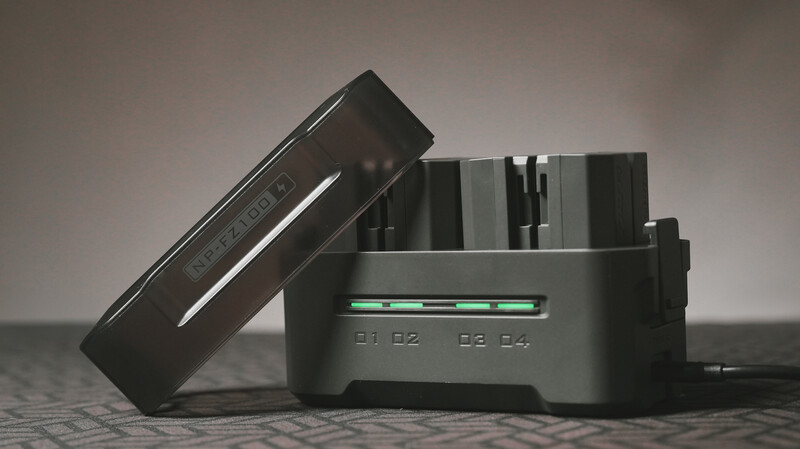 Professional camera battery charger with four charging slots and indicator lights, positioned with its lid propped open.
