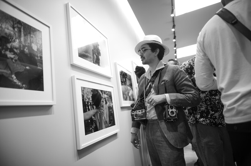 Man with cameras looking at photographs in an art gallery