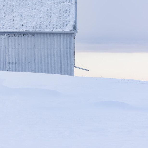 Minimalist winter landscape with a corrugated metal structure against snow and overcast sky.