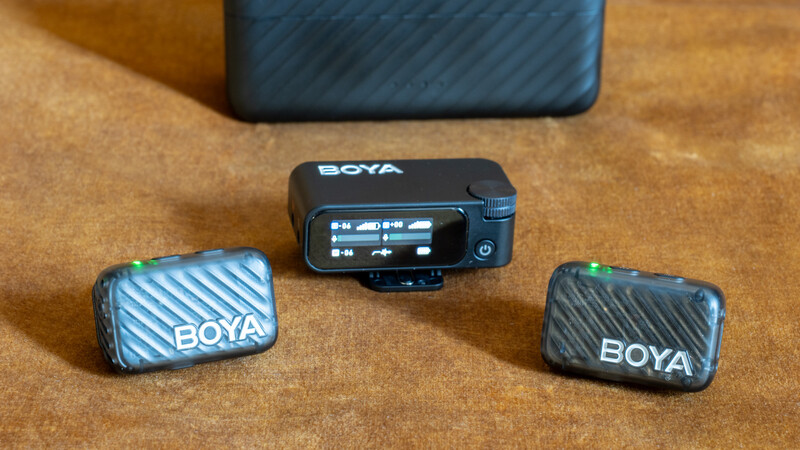 BOYA wireless microphone system with receiver unit and two transmitter modules arranged on a wooden surface.
