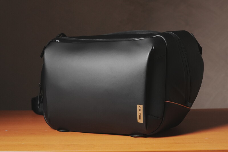 Black camera bag with padded exterior and orange accent stripe on wooden surface.