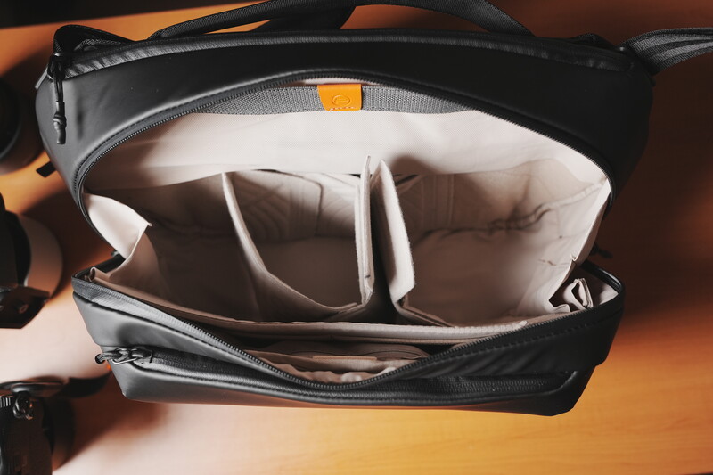 Open camera bag with white fabric dividers and compartments against warm orange lighting.