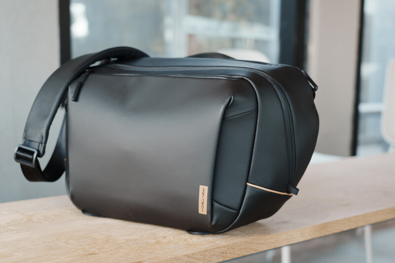Black camera bag with shoulder strap on wooden table in office setting.