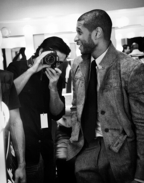 Photographer holding a camera at what appears to be an indoor event or gallery space.
