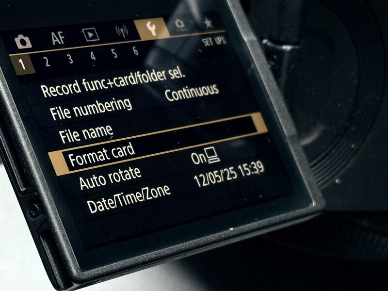 Screenshot of camera menu displaying Record function, card holder settings, file numbering options, and date/time zone configuration.