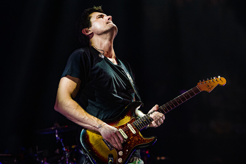 Guitarist performing on stage with a sunburst Stratocaster-style electric guitar, head tilted back in expression.