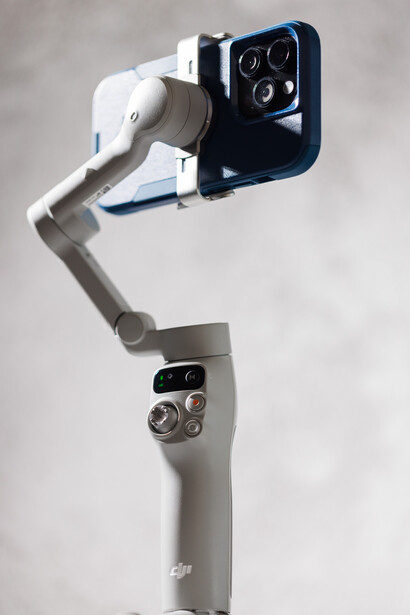 Three-axis motorized gimbal stabilizer with smartphone mount holding a mobile device with multiple camera lenses.