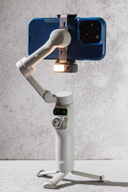 DJI OM gimbal with smartphone mounted on articulating arm against textured backdrop.