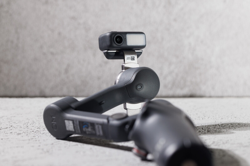 Gimbal stabilizer with mounted camera positioned on concrete surface against gray textured wall.