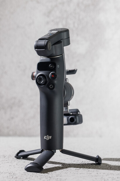 DJI smartphone gimbal stabilizer mounted on a compact tripod stand against a textured gray wall.