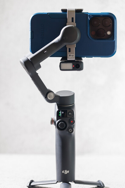 DJI smartphone gimbal stabilizer with blue phone mount secured on tripod stand.