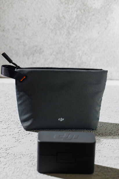 DJI drone carrying case and battery pack positioned on concrete surface against white wall.