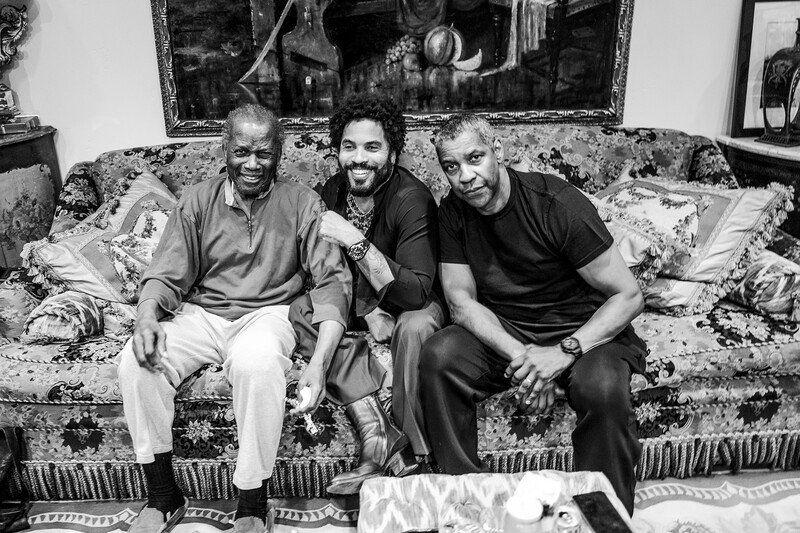 Three men sitting together on a patterned sofa, smiling at the camera in a black and white portrait.