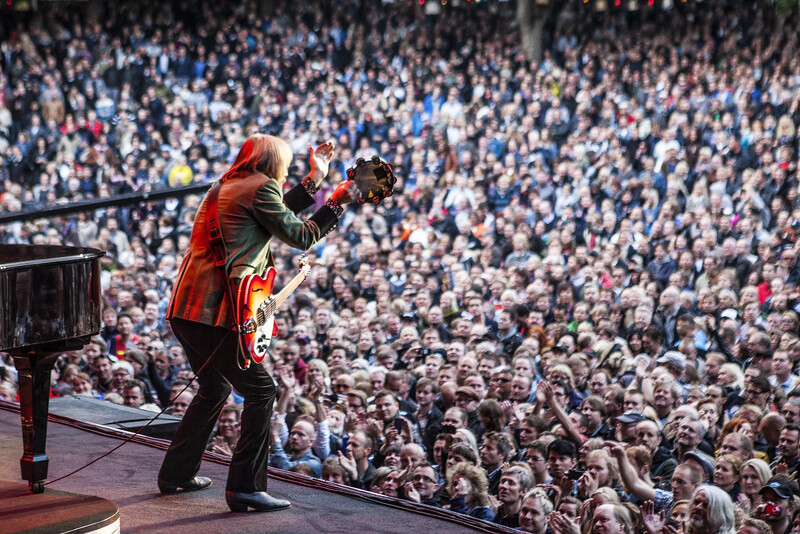 Performer in red jacket on stage addressing large crowd in arena venue.