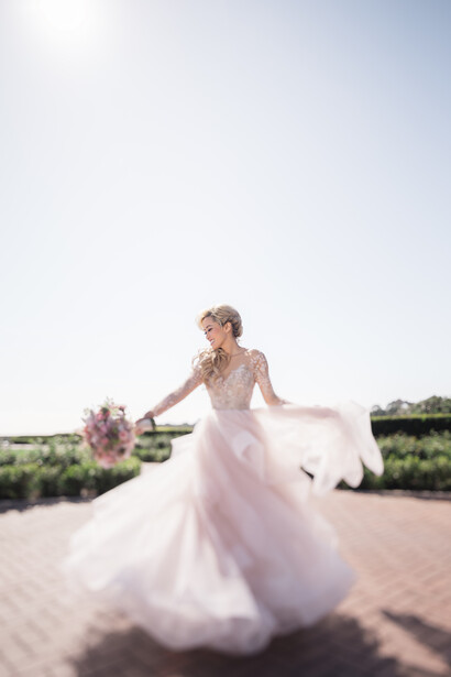 Bride in flowing white gown twirling outdoors with bouquet, dramatic train in motion.