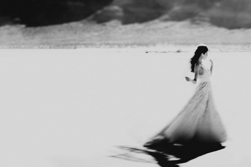 Woman in flowing wedding dress walking across a vast, snowy landscape in black and white.