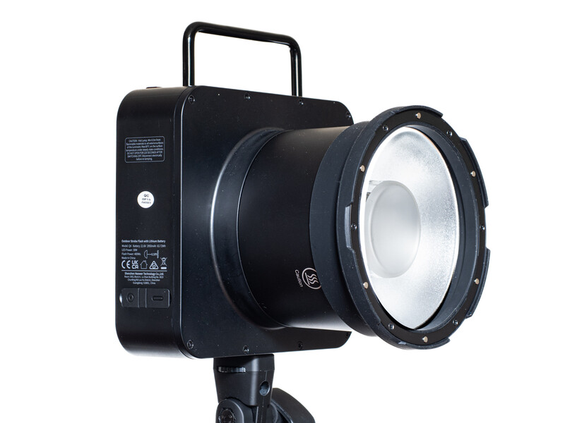Black studio light with circular fresnel lens mounted on tripod against white background.
