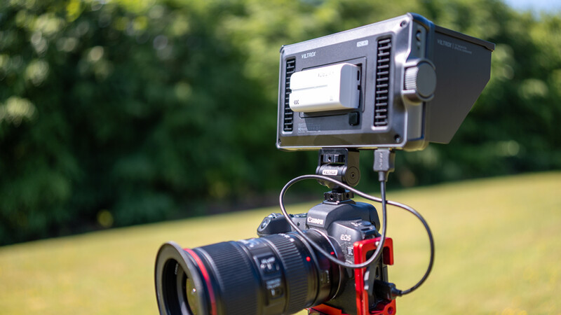 Professional video light mounted on camera rig with telephoto lens outdoors.