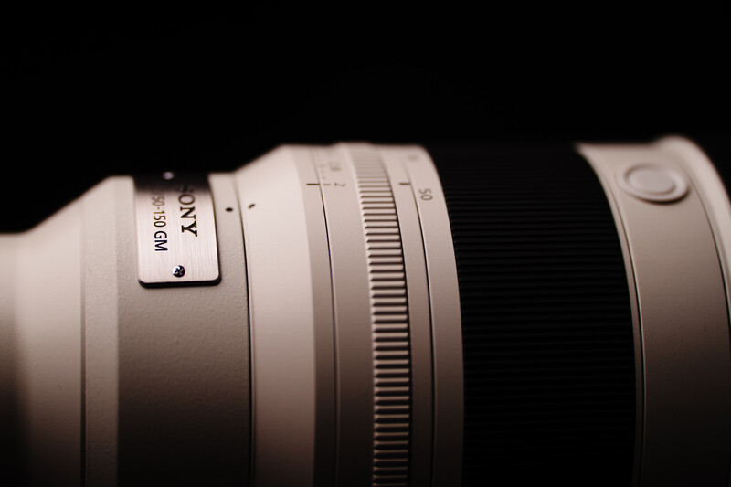 Close-up of a white telephoto lens barrel with focus and zoom rings against a dark background.