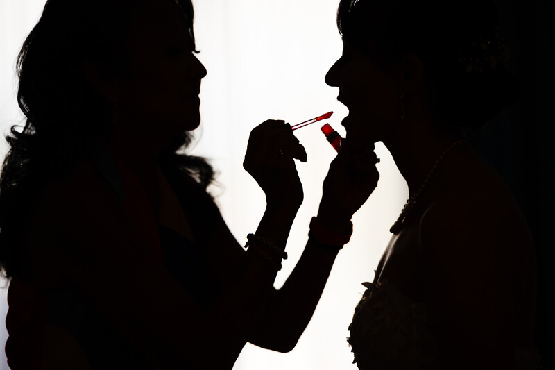 Silhouette of a makeup artist applying lipstick to a client's face against a bright backlit background.