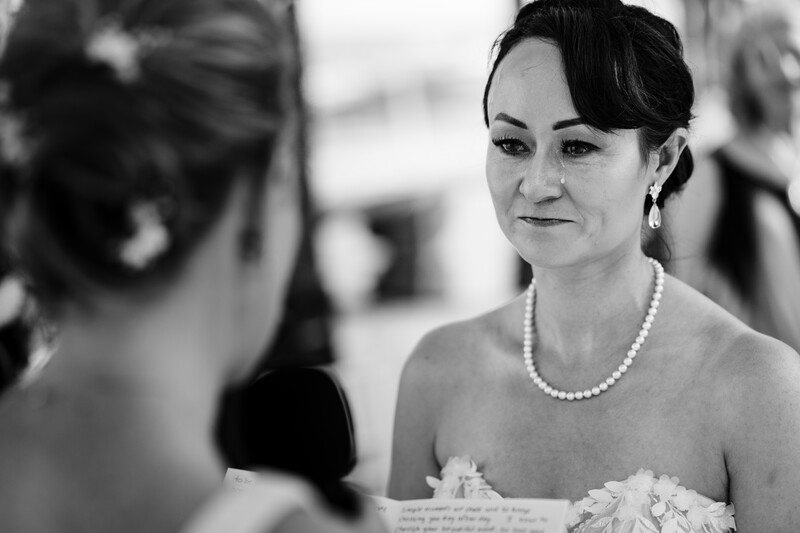 Bride in strapless white dress and pearl necklace gazes thoughtfully during wedding ceremony.