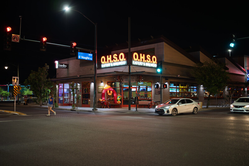 Nighttime storefront with O.H.S.O. signage and parked white car on street.