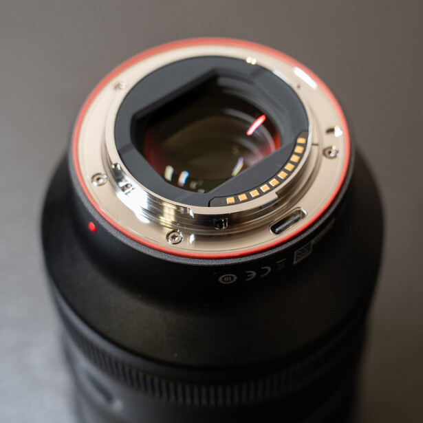 Camera lens mount with red gasket seal and glass elements visible through opening.