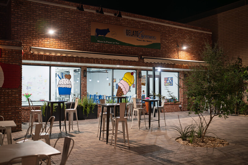Nighttime exterior shot of a brick storefront with illuminated windows and outdoor seating area.
