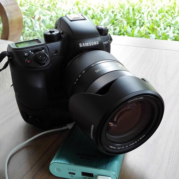 Samsung NX1 mirrorless camera with telephoto lens mounted, positioned on a blue power bank.