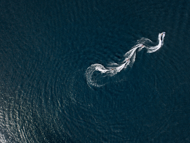 Aerial view of a ship's wake creating a white serpentine pattern across dark ocean water.