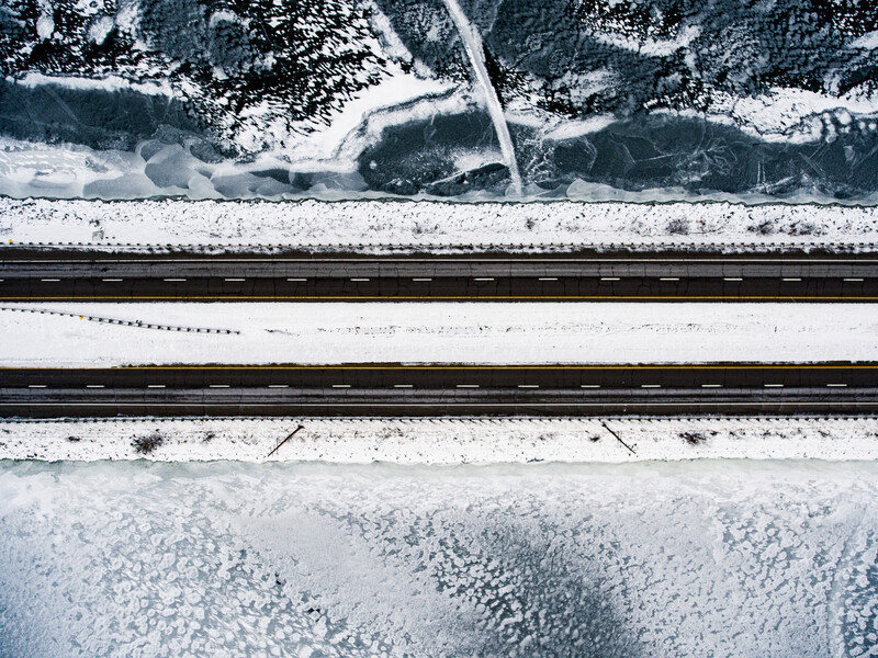 Aerial view of snowy landscape with railroad tracks running through center and forested areas along the sides.