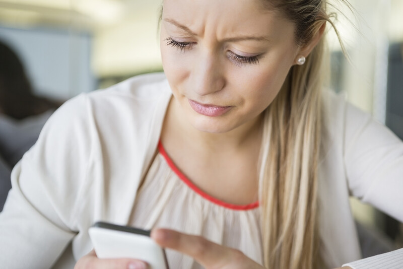 Woman looking at smartphone with concerned expression and furrowed brow.