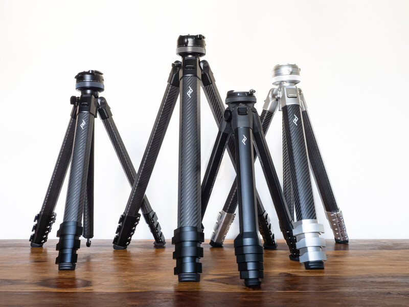 Four carbon fiber camera tripods of varying heights arranged in a row on a wooden surface.