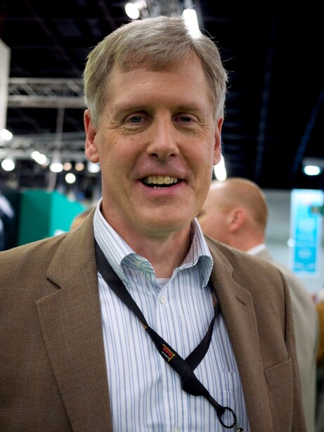 Man in tan blazer and striped shirt smiling at an event venue.