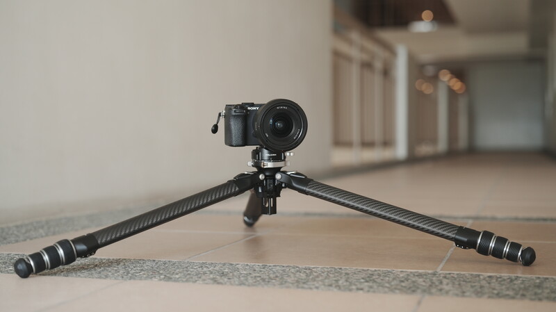 Mirrorless camera mounted on a tripod with extended legs in an indoor hallway.