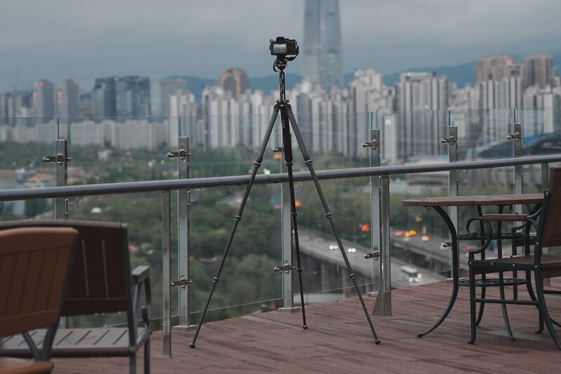 Professional camera mounted on tripod on rooftop overlooking dense urban skyline with skyscrapers.