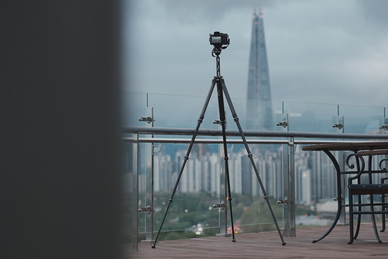 Professional camera on tripod mounted on a high-rise balcony overlooking a city skyline.