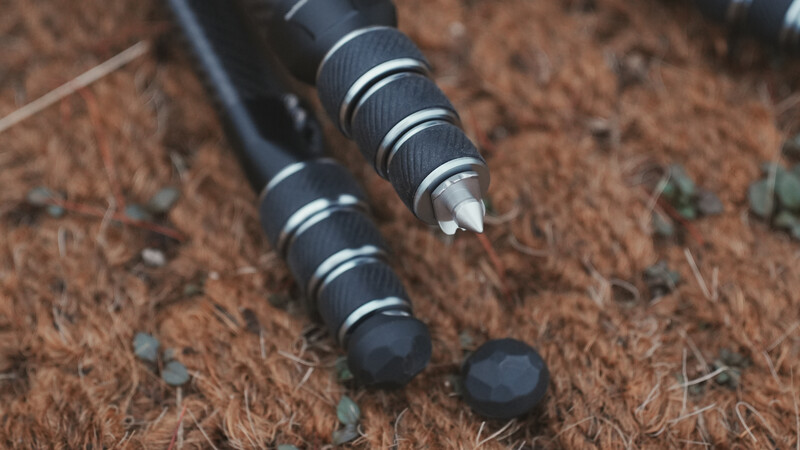 Close-up of tripod leg feet with textured rubber grips and metal bands on sandy ground.