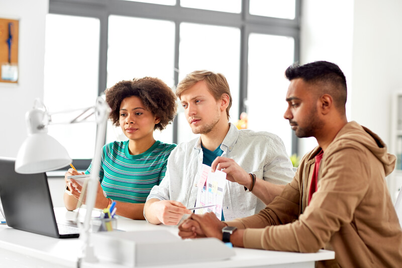 Three people collaborating at a desk with a laptop and documents in a bright office space.
