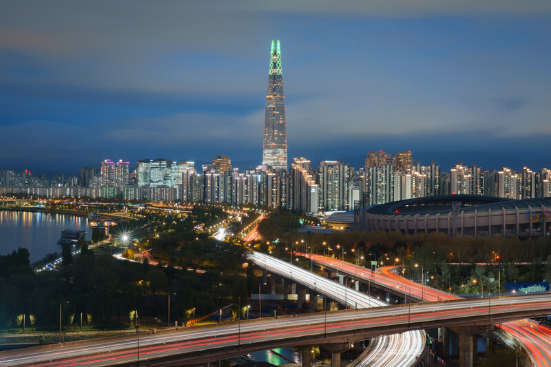 Illuminated cityscape at dusk with tall tower and elevated highway interchange in foreground.