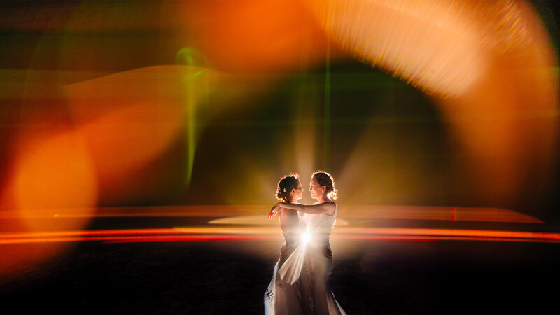 Bride and groom silhouetted against warm golden-orange backlighting on a dark horizon.