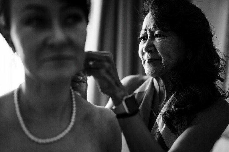 Woman adjusting another woman's pearl necklace in black and white portrait.