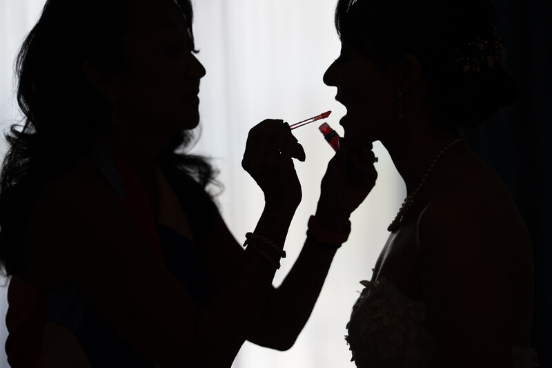 Silhouetted figure applying makeup to another person's face against backlit background.