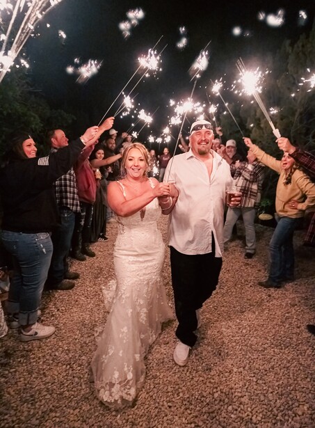 Bride and groom walking through a tunnel of sparklers held by wedding guests at night.