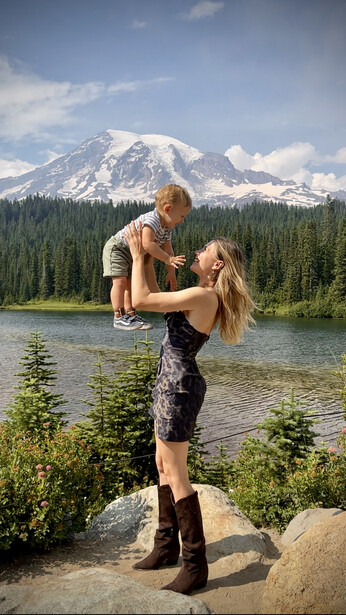 Man holding a young child while standing on a rock beside a mountain lake.