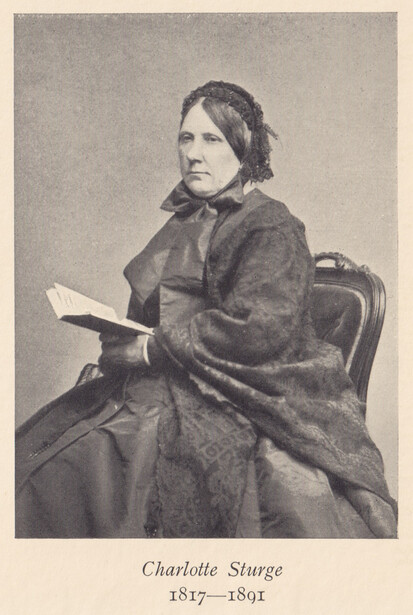 Portrait photograph of a woman seated in a chair, holding an open book, wearing dark clothing with a bow at the neck.