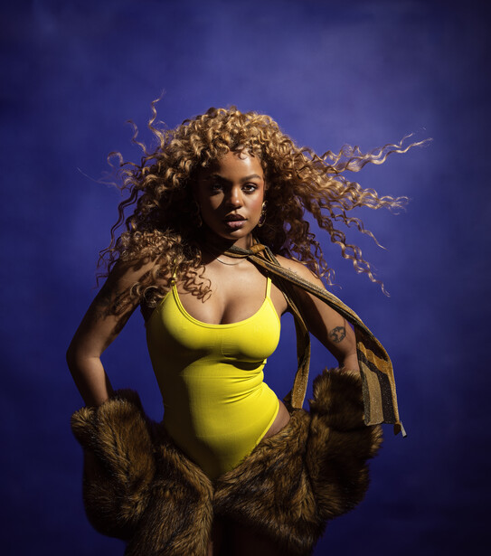 Woman in yellow swimsuit with curly blonde hair against deep blue background.