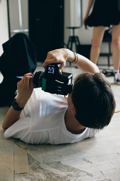 Photographer lying on concrete floor composing shot through smartphone camera while holding device overhead.