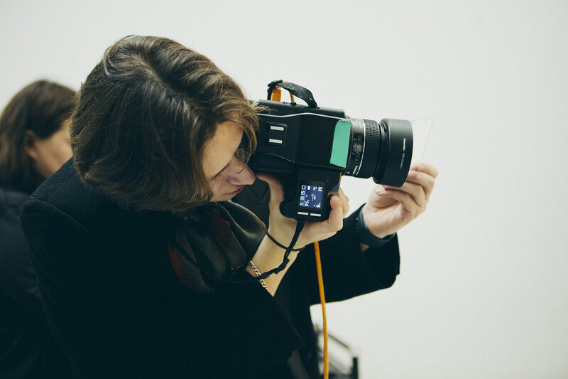 Photographer holding a vintage film camera with a telephoto lens and light meter attachment.