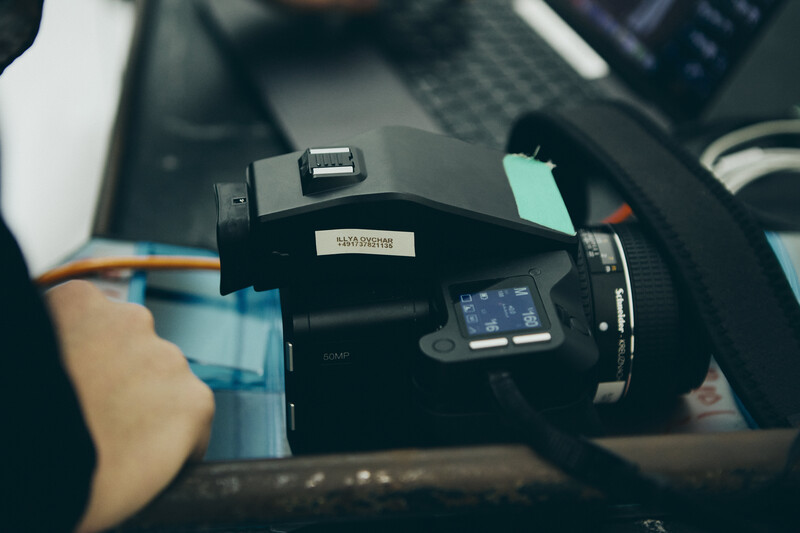 Overhead view of a mirrorless camera with external flash mounted on top, surrounded by photography gear on a dark workspace.